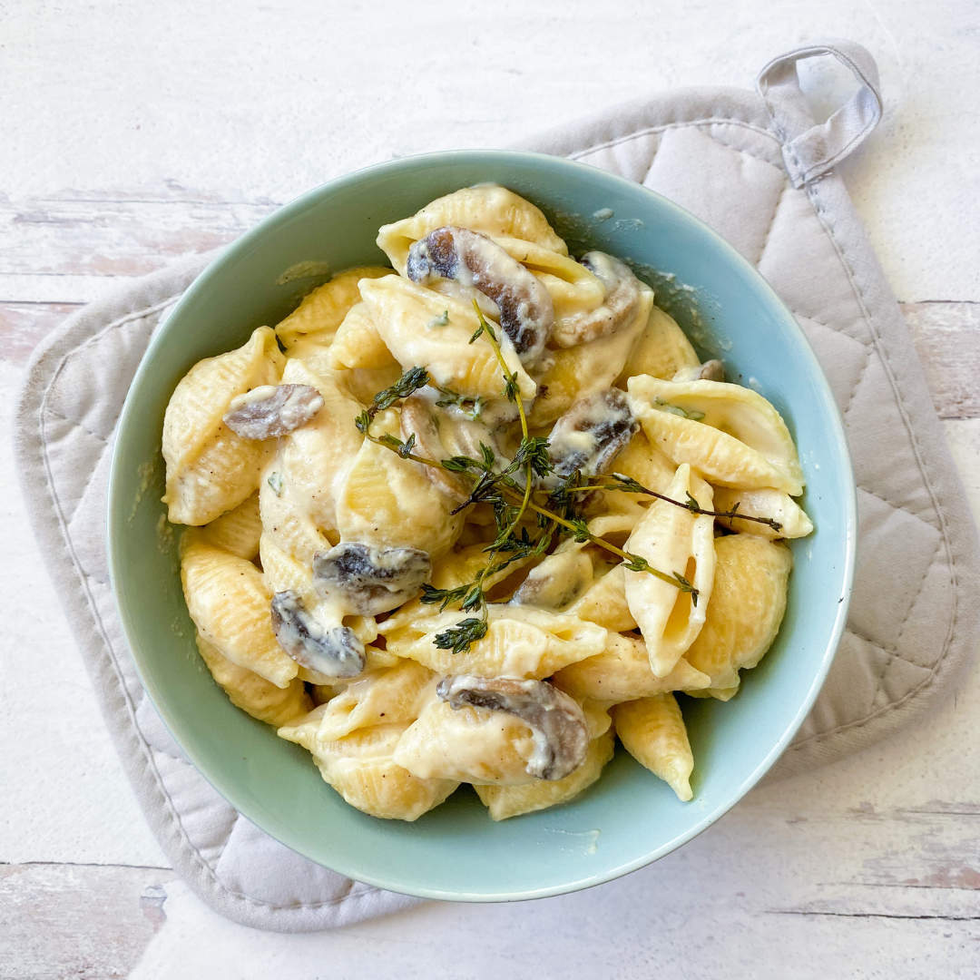 Vegan Alfredo Sauce in bowl of shell pasta with mushrooms and fresh thyme